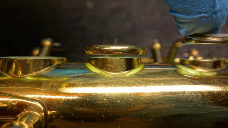 A pad cup in the proper orientation, level and centered over the tonehole with the appropriate distance from the tonehole to the back of the key cup for a .160" pad and a thin layer of adhesive.  This is a gold plated 1932 Selmer, and not a single one of the pad cups started off this way!  Selmers are interesting in that from the factory they are actually set up for graduated thickness pads (thinner up top and getting thicker toward the bottom of the horn), and unless a repairer is aware of this typically every pad cup will get bent to use one thickness, typically .185, which is too thick for the upper stack.